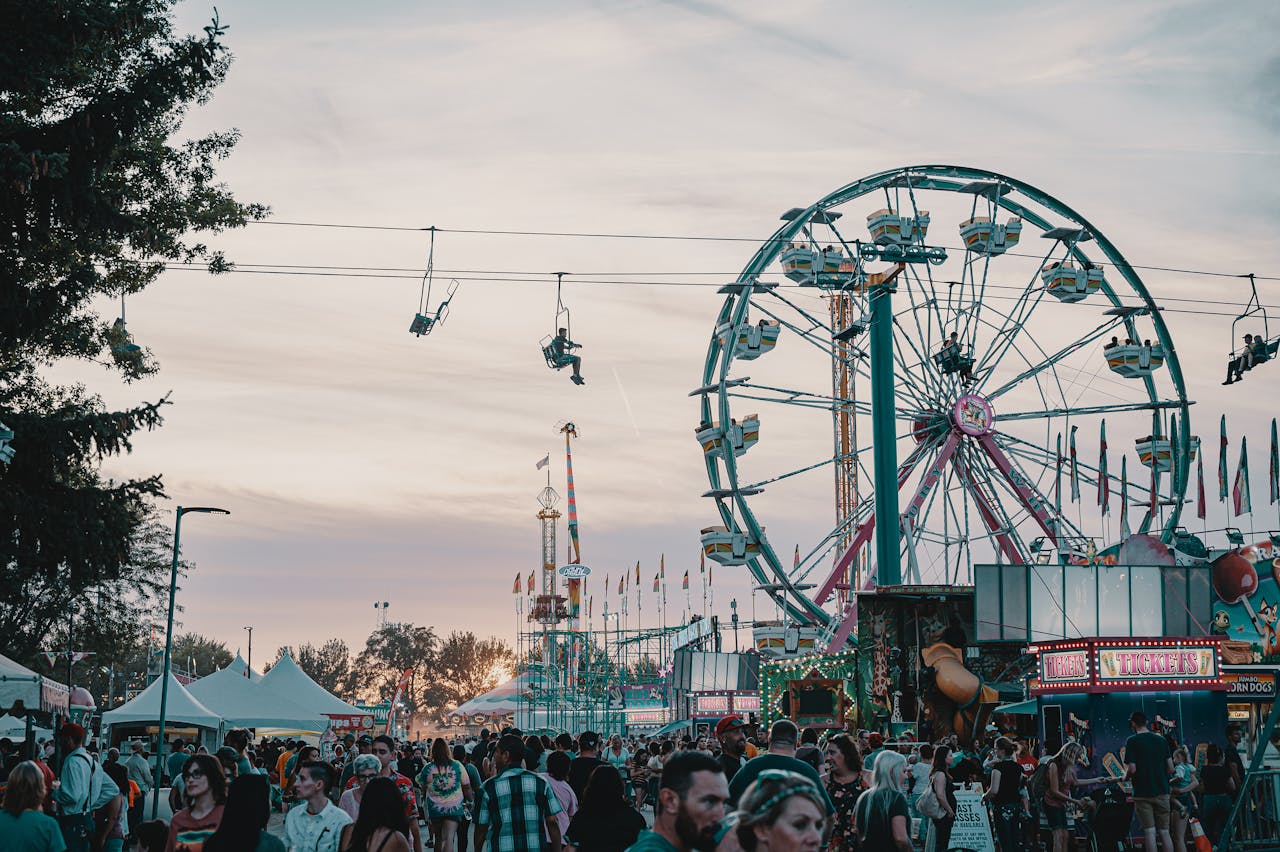 Services-01 Crowd enjoying an amusement park with Ferris wheel and rides at sunset.
